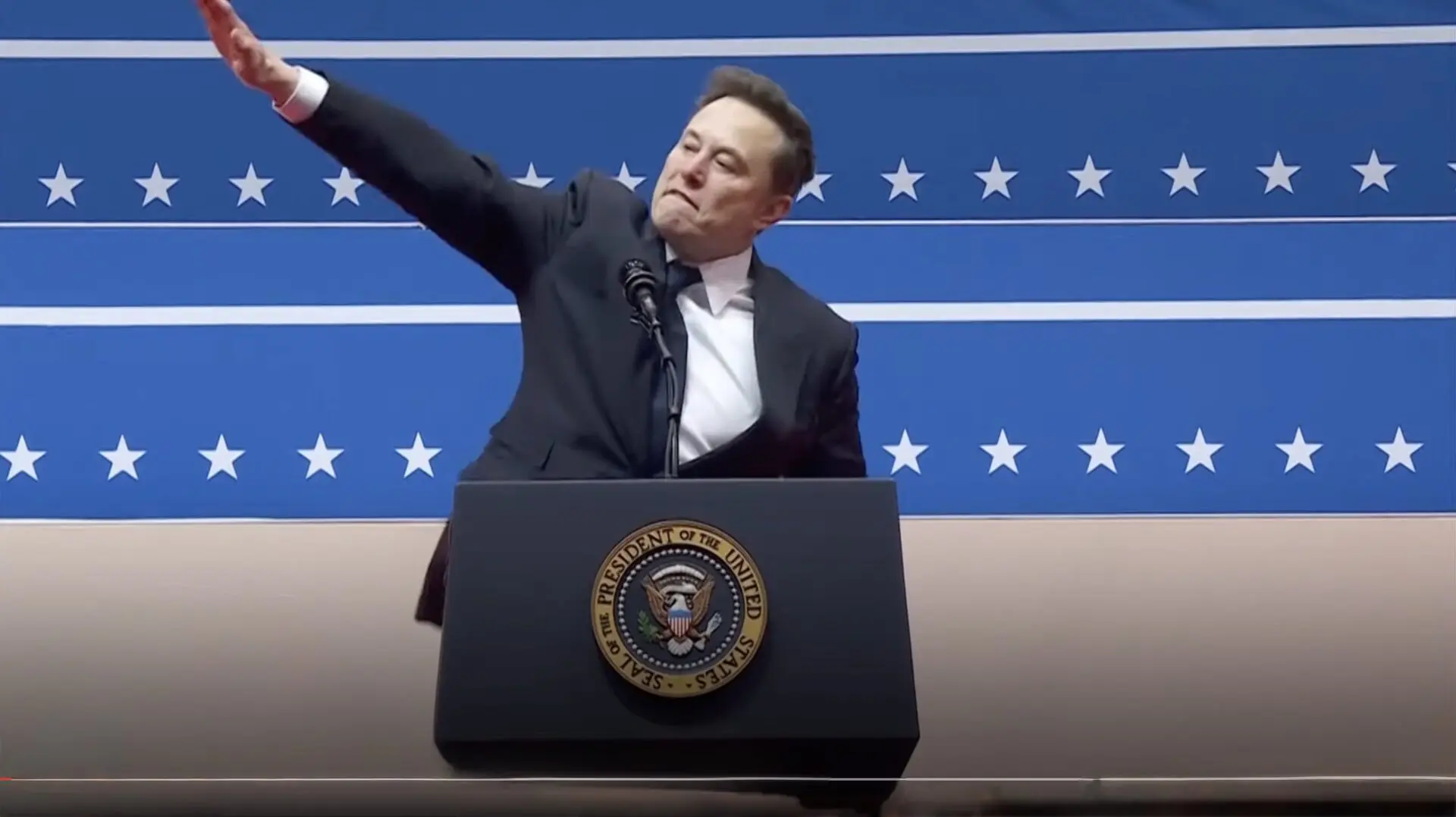 Elon Musk levanta el brazo durante un discurso en un escenario con emblemas patrióticos, frente al sello presidencial de Estados Unidos.